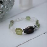 Close-up of a stylish bracelet on a white wooden surface, showcasing green and brown beads.