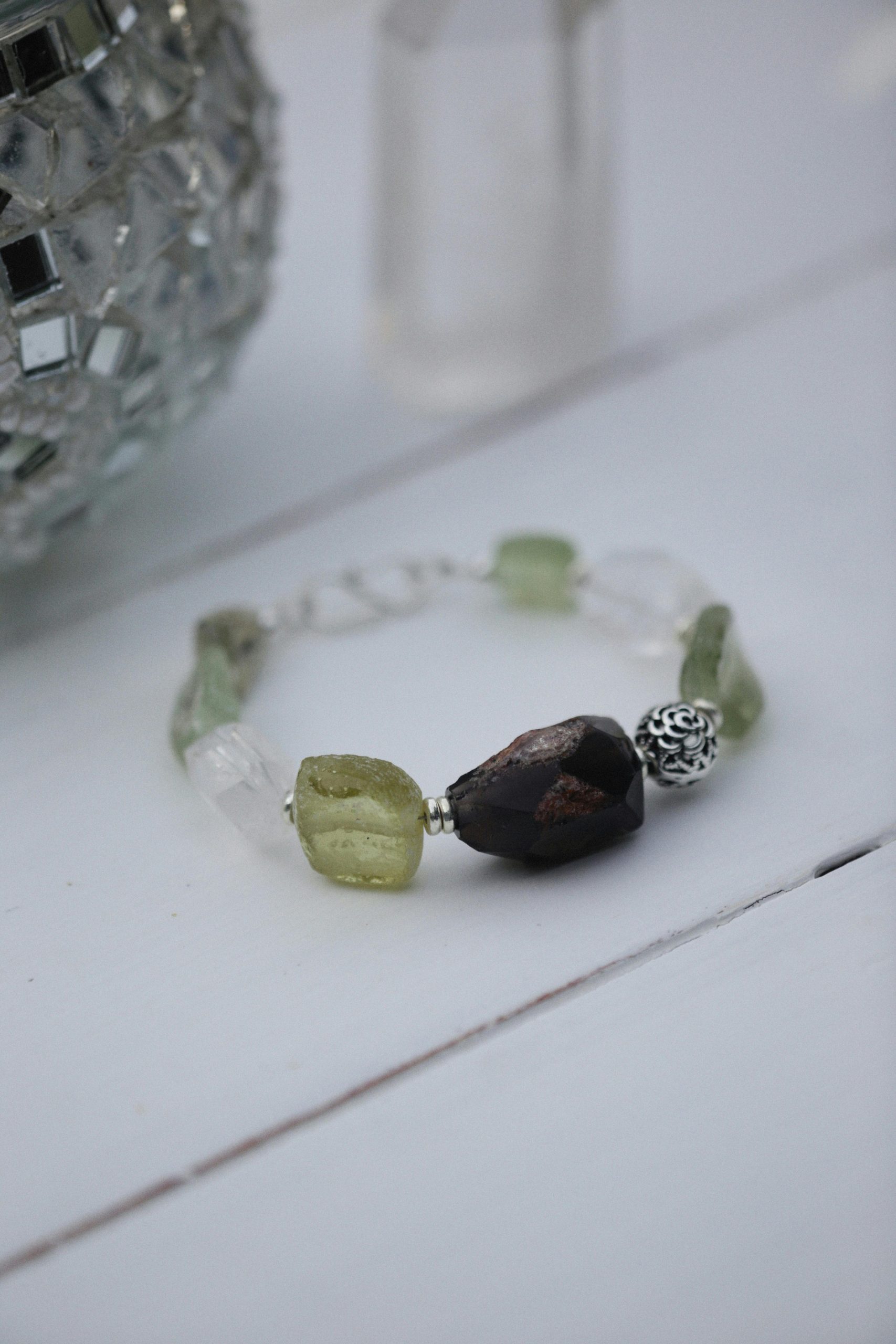 Close-up of a stylish bracelet on a white wooden surface, showcasing green and brown beads.