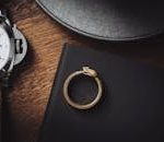 Close-up of a stylish snake ring and luxury wristwatch on a dark wooden surface.