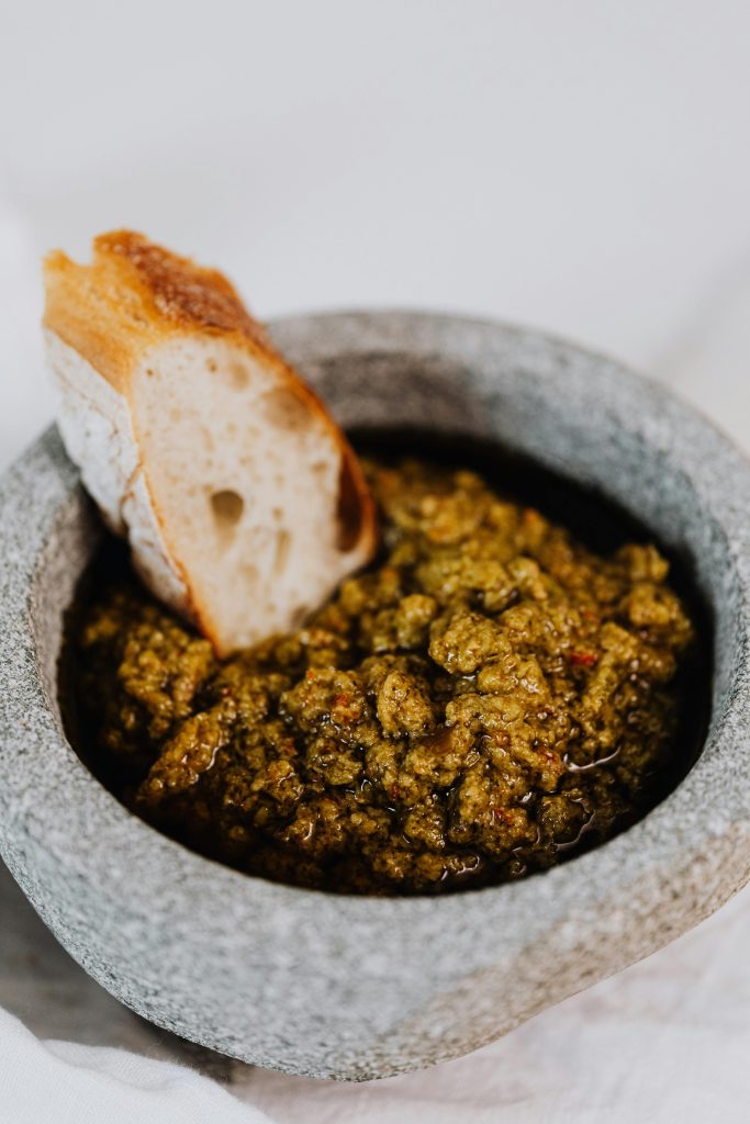 Close-up of fresh pesto dip with crusty bread in a stone mortar.