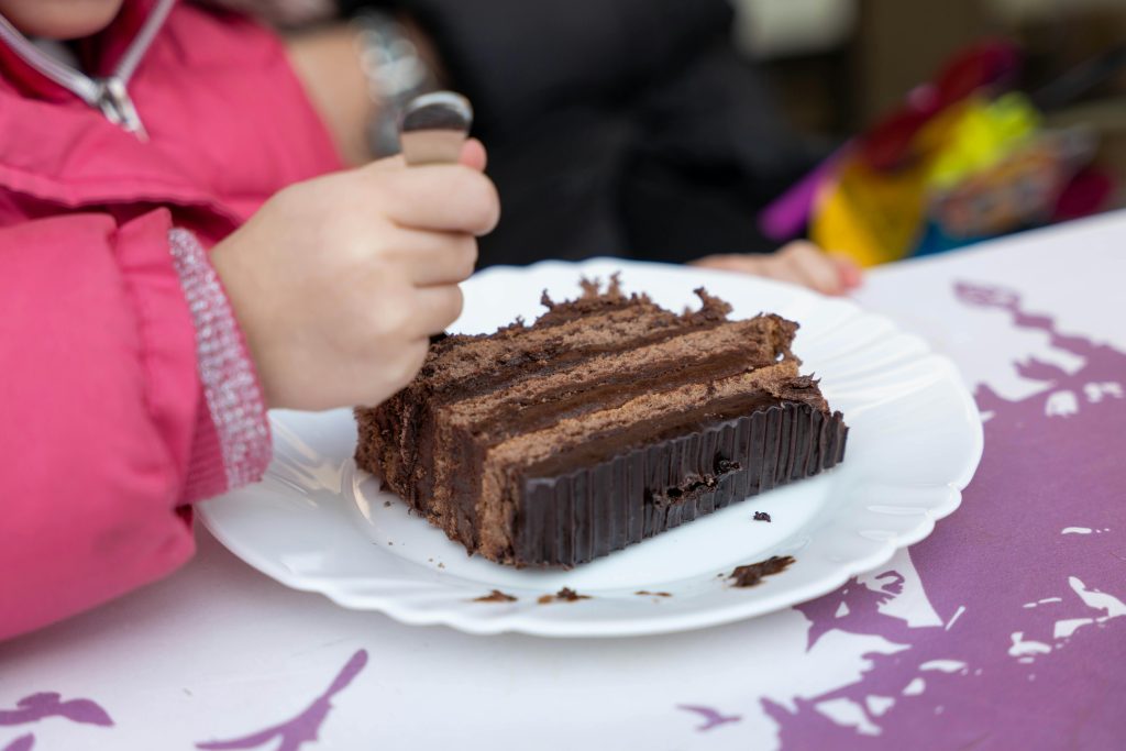 A child savors a piece of rich chocolate cake on a white plate indoors.