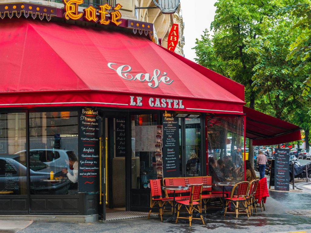 A picturesque view of a traditional Parisian café with a red awning and outdoor seating, ideal for experiencing French culture.