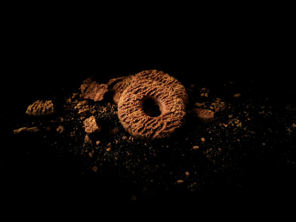 Moody close-up of chocolate cookie with crumbs on a dark background, capturing indulgence and texture.